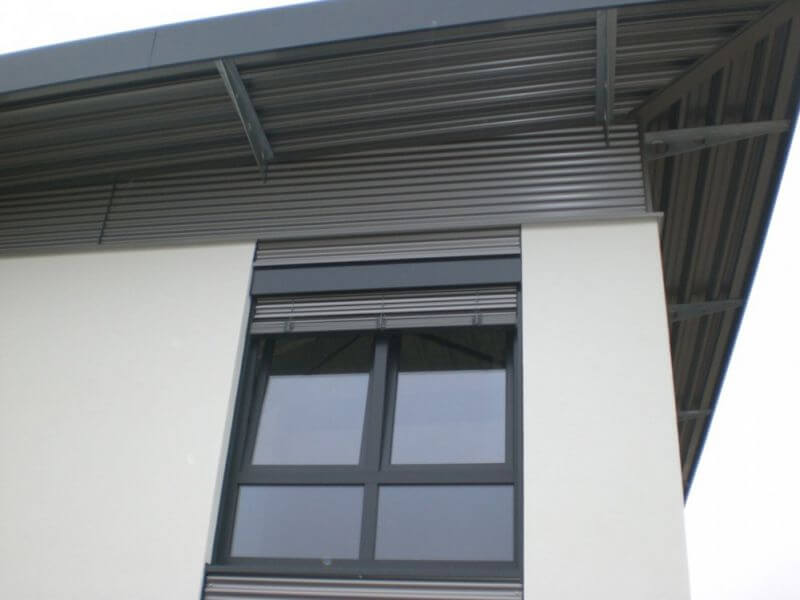 Der Sonnenschutz integriert sich perfekt in die Verkleidung mit einer Stahlwelle, die auch der Dachüberstand (Vordach) verkleidet. Gleichzeitig schützt der Überstand vor Regen, Fensteröffnung auch bei Regen möglich.
